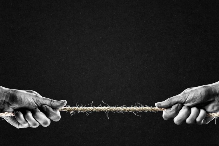 Two hands pulling on opposite ends of a frayed rope against a dark background, suggesting tension or struggle.